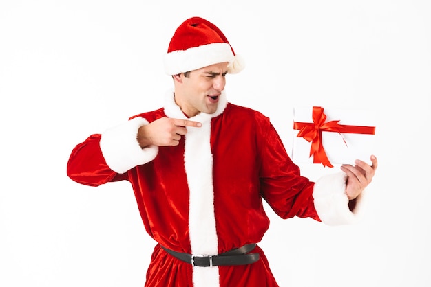 Portrait of surprised man 30s in santa claus costume and red hat holding present box