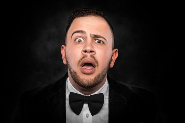 Portrait of surprised man in suit with bow-tie over dark background.