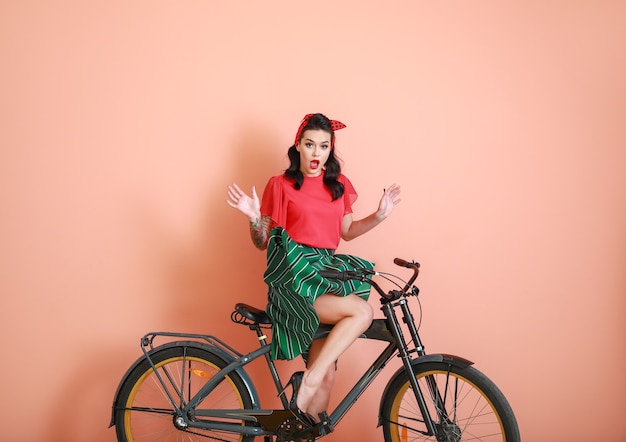 Portrait of surprised tattooed pin-up woman riding bicycle on color