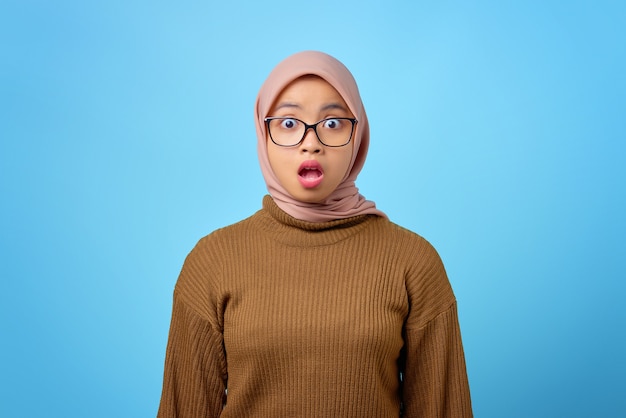 Portrait of surprised young Asian woman with open mouth on blue background