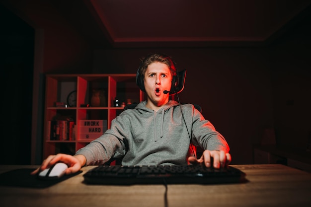 Portrait of a surprised young male gamer in casual clothes and headset sitting in a room