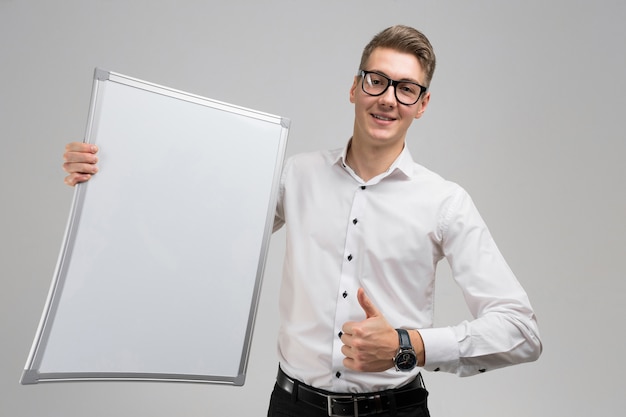 Portrait of surprised young man in glasses with clean Board and shows sign super 