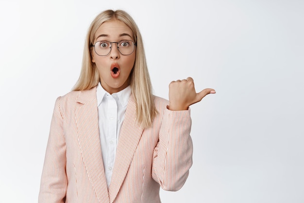 Portrait of surprised young woman gasping pointing finger right looking impressed by advertisement sale promo white background