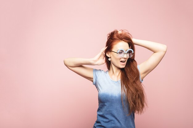 Portrait of surprised young woman in sunglasses enjoying in front of pink wall.