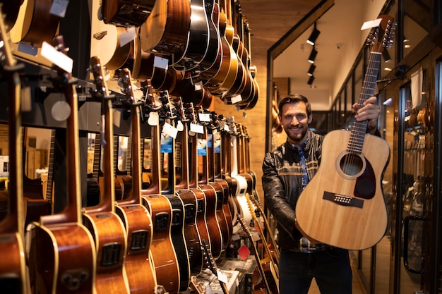 Portrait of talented caucasian musician in leather jacket standing in music shop and holding classic acoustic guitar for sale.