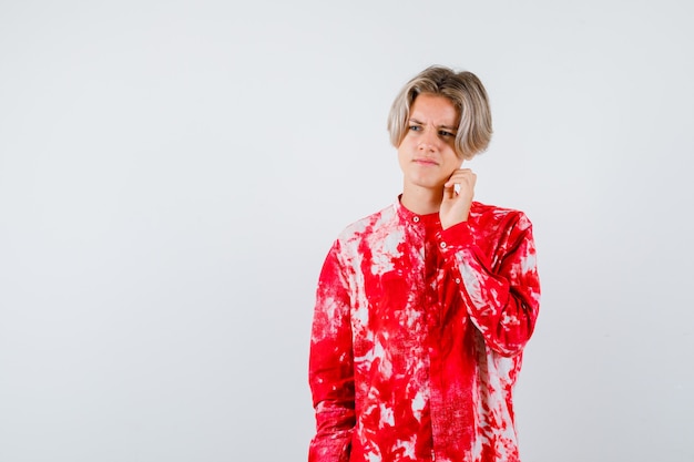 Portrait of teen blonde male with hand near face in oversize shirt and looking upset front view