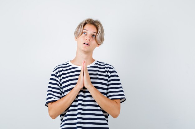 Photo portrait of teen boy keeping hands in praying gesture in t-shirt and looking hopeful front view