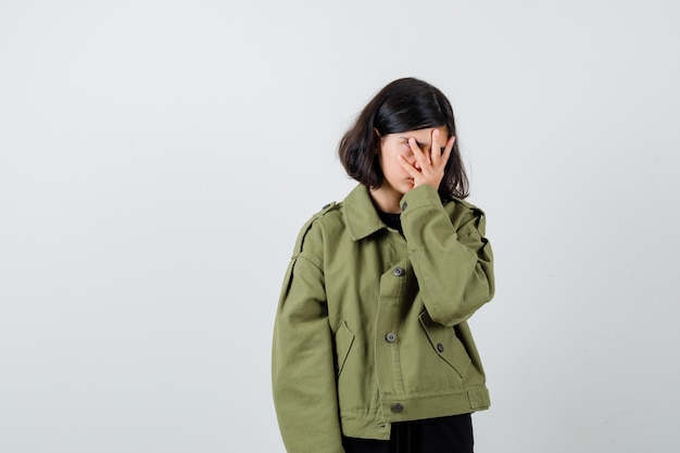 Portrait of teen girl holding hand on face in army green jacket and looking exhausted front view