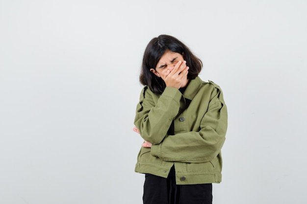 Portrait of teen girl holding hand on mouth in army green jacket and looking sorrowful front view