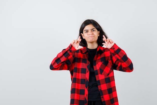 Portrait of teen girl showing crossed fingers in casual shirt and looking hesitant front view