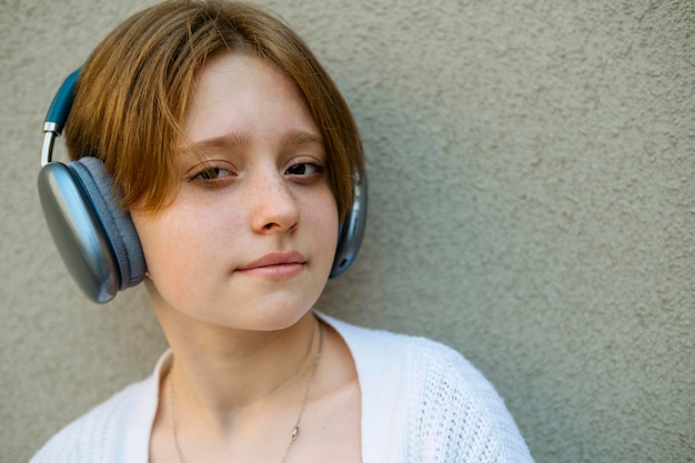 Portrait of a teenage girl in headphones against a gray wall