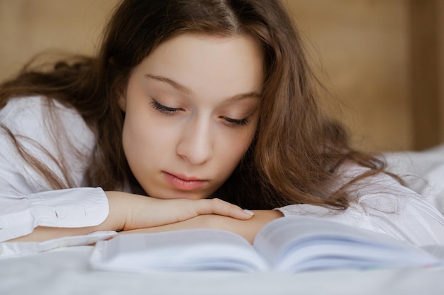 Portrait of the Teenage girl reading a book lying on the bed