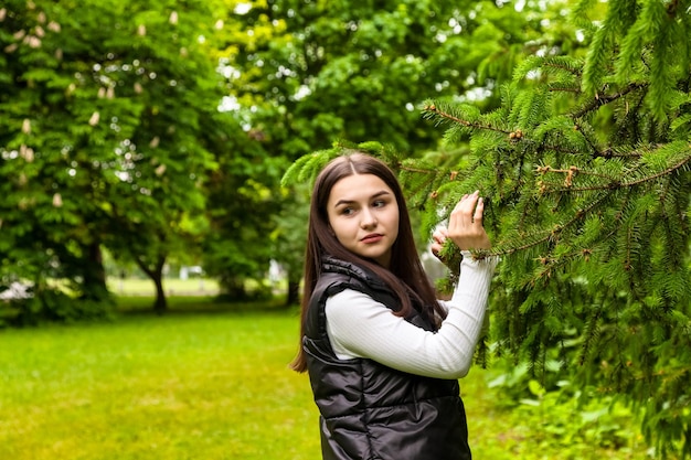 Portrait teenage girl walking in spring park in green fir trees or spruce