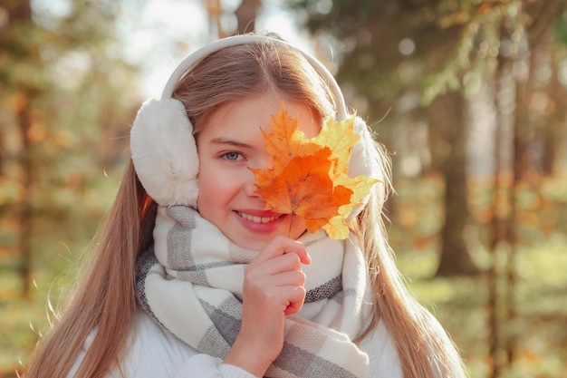 Portrait teenage girl with fall leaves looking at camera wearing casual clothes in an autumn park outdoors