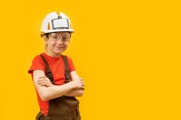 Portrait of teenager wears protective helmet glasses and jumpsuit like worker or construction worker on yellow background Copy space