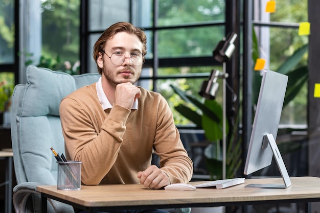 Portrait of thinking serious man with computer inside modern green loft office blond man looking