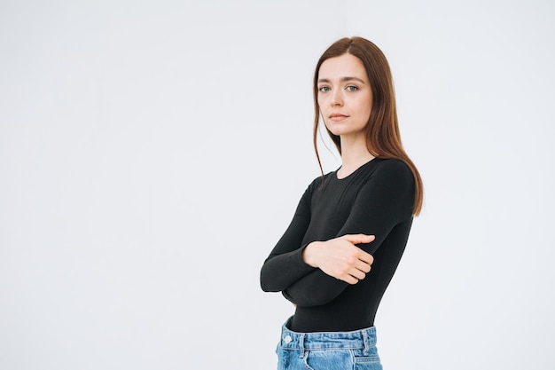 Portrait of thinking young beautiful woman in close pose with dark long hair in black longsleeve and jeans on the white background isolated