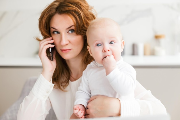 Portrait of thoughtful business woman sitting and talking on her cellphone while holding her cute little baby in hand