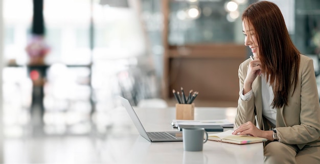 Portrait of thoughtful young asian businesswoman in suit sitting at office desk