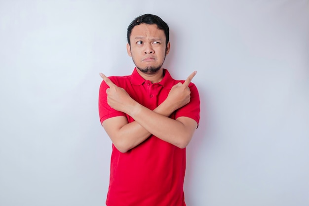 Portrait of a thoughtful young casual man wearing a red shirt pointing upside isolated over white background