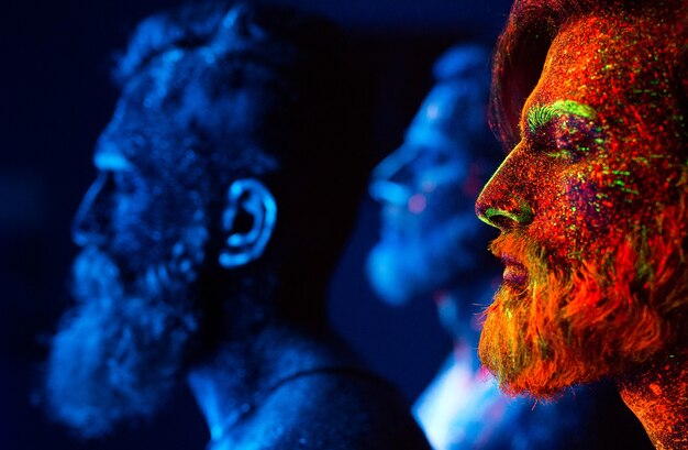 Portrait of three bearded men painted in florescent powders.