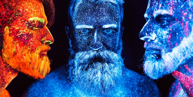 Portrait of three bearded men painted in florescent powders.