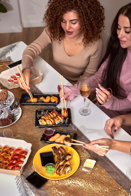 Portrait of three beautiful young women eating japanese food and drinking wine at home