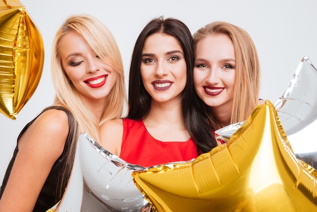 Portrait of three cheerful attractive young women with star shaped balloons over white background