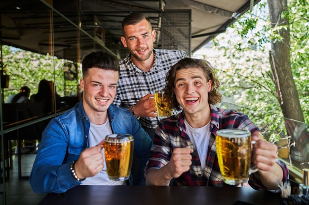 Portrait of three friends drinking beer in pub.