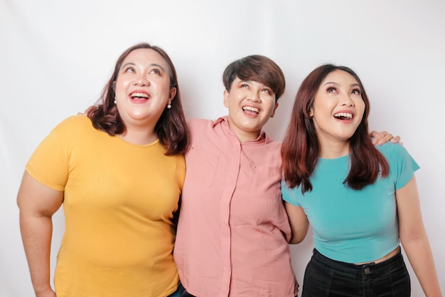 A portrait of three friends looks excited pointing at the copy space upside them isolated by white background