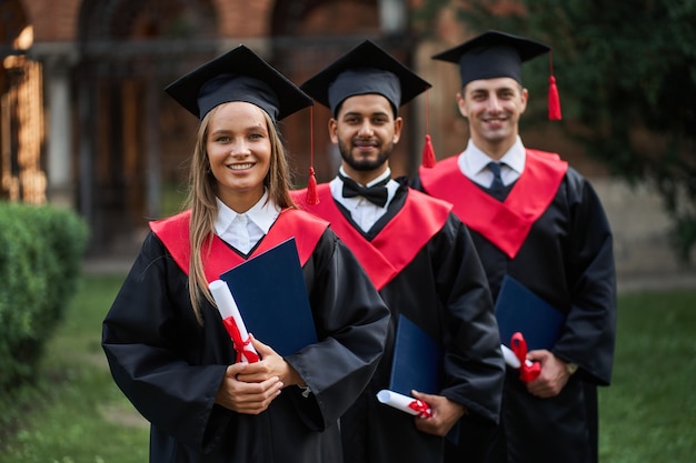 Portrait of three happy graduates in graduation gowns and diploma.