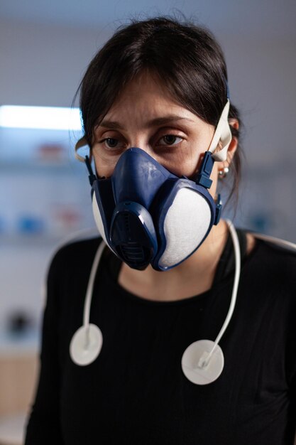 Portrait of tired athlete woman wearing medical electrodes working at body endurance. Sportwoman with mask training on cross trainer increasing rhythm of exercises in clinical laboratory