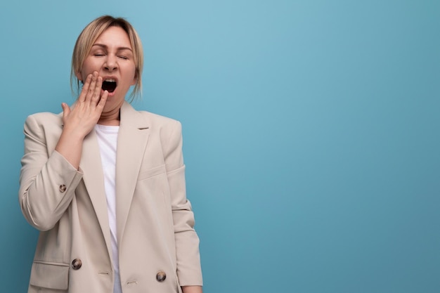 Portrait of a tired blonde young woman in a creamcolored jacket working in the office on a blue