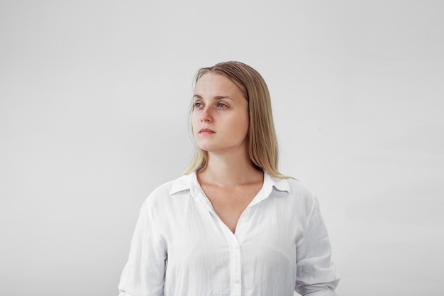 Portrait of a tired girl without makeup on a white wall