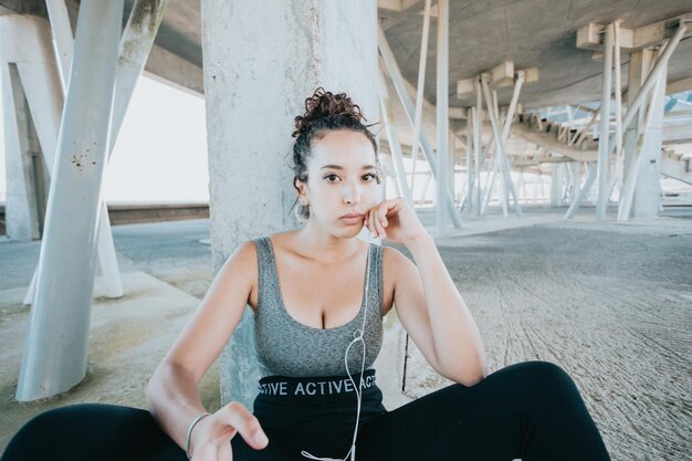 Portrait of tired looking serious young african woman taking a break after workout exercises. athlete female in sportswear relax hearing music on his phone. Urban sport .Leggings clothing and top.