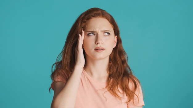 Portrait of tired redhead girl showing headache on camera over colorful background