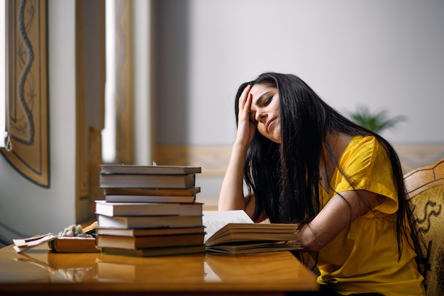 Portrait of a tired student girl studying with books at the old library