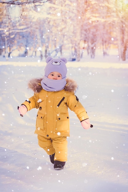 Portrait of toddler 1217 months old in yellow winter clothes walking in the park during a light snowfall