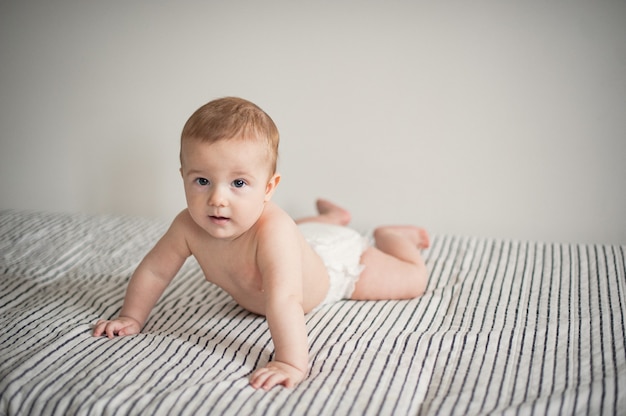 Portrait of a toddler in a diaper lying on a striped light blanket