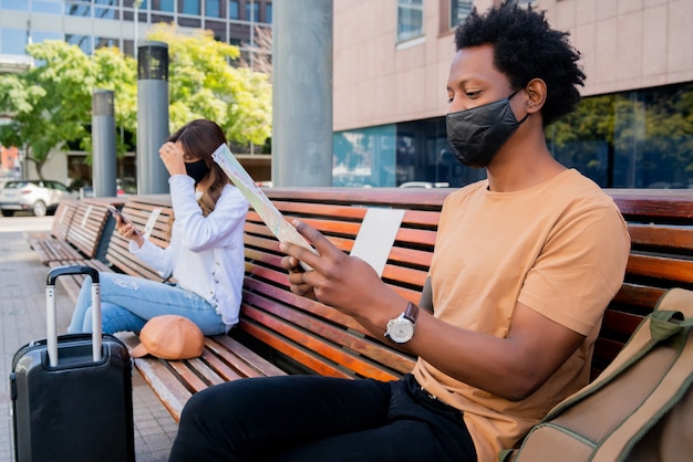 Portrait of a tourist people waiting outside airport or train station while sitting on bench and keeping distance