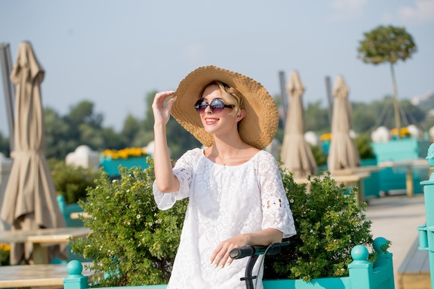 Portrait of Trendy woman, beautiful blonde girl in white dress, sunglasses and hat riding scooter