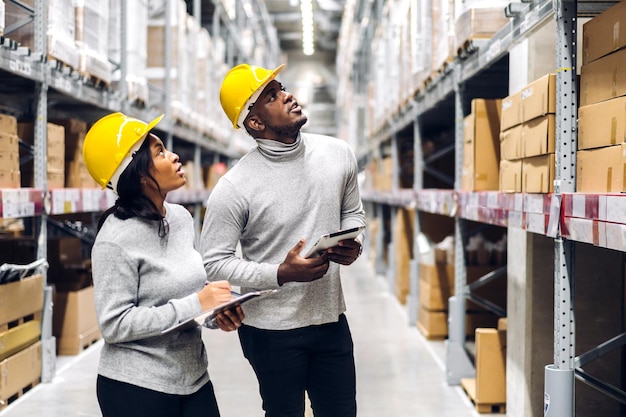 Portrait two african american engineer team shipping order detail on tablet check goods and supplies on shelves with goods inventory in factory warehouselogistic industry and business export