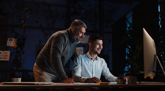 Portrait of two attractive male colleagues working on the computer on a joint project long into the