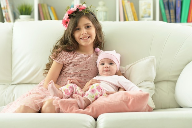 Portrait of two beautiful cute sisters posing in sofa at home