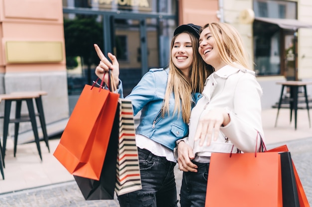 Photo portrait of two blondes in the middle of the street shopping, one of them points to the discount stores