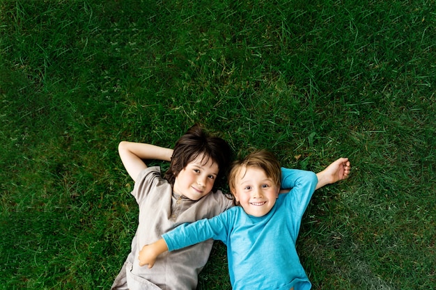 Portrait of two brothers lying on a grass in a park. Smiling happy children outdoors. Siblings friendship.