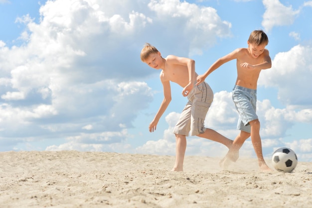 Portrait of two brothers playing football on beach in summer day