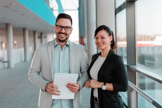 Portrait of two business people standing in office lobby.