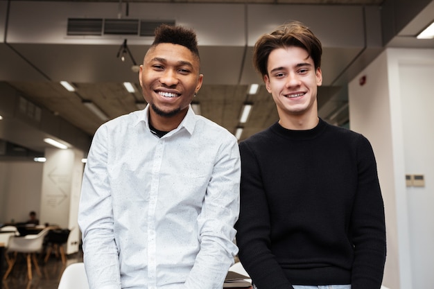 Portrait of two cheerful handsome students standing in library.