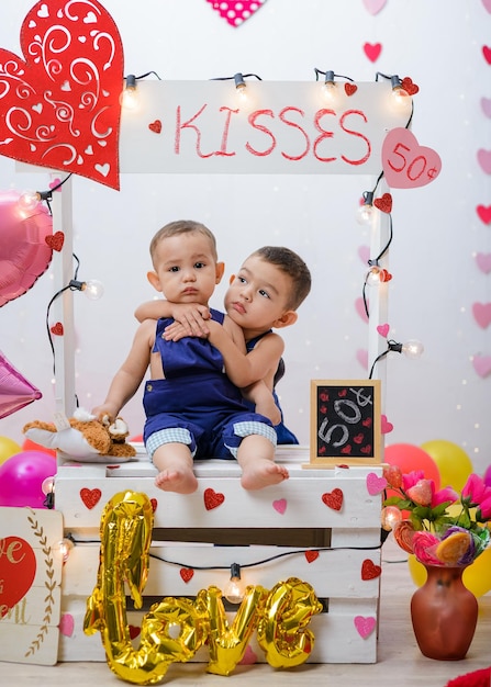 Portrait of two children in a kissing booth decorated with hearts and balloons